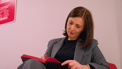 businesswoman smiling and writing in red notebook with red pen in office. focus on professional work, planning, and note-taking in modern workspace. relaxed atmosphere, creative, and productive