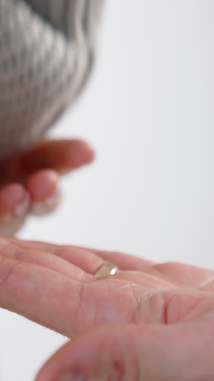 Hand of a little unrecognized baby wearing a grey sweater. Infant's hand is on the male adult hand. Close up. White backdrop. Vertical video