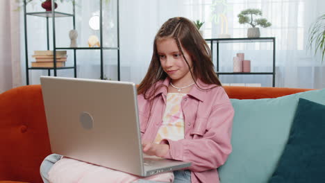 girl child opening and using laptop watching movies study education while sitting on home couch