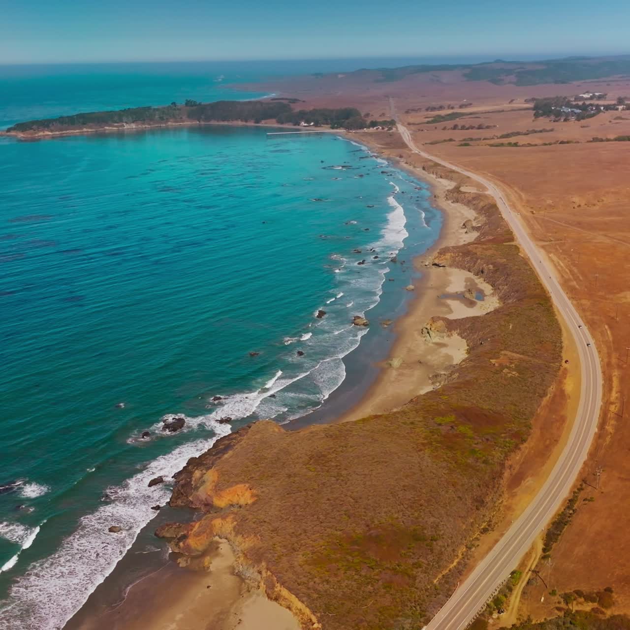 Dry deserted land bordering with blue waters of ocean. Highway through the coastline of Morro Bay, California, USA. Top view