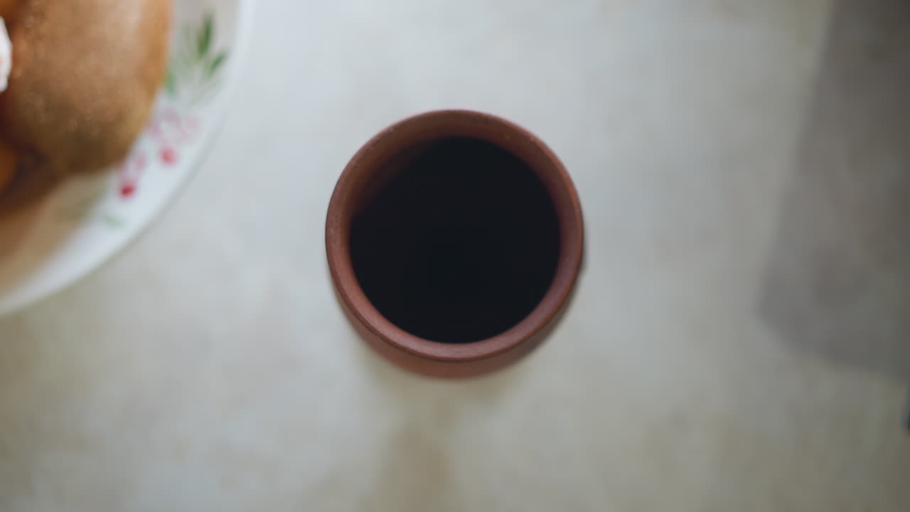 Tazza di caffè e piatto di pane dall'alto, rituale mattutino del cuoco casalingo con tazza di ceramica calda, luce solare soffusa, piano del tavolo texturizzato, atmosfera rustica accogliente, semplice scena della colazione che mostra una bevanda fumante