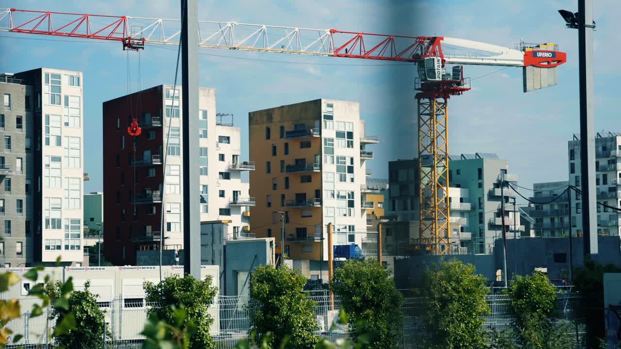 Una gran grúa de construcción se eleva sobre los modernos edificios residenciales de varias plantas en Nantes, mostrando el crecimiento urbano y el desarrollo arquitectónico con árboles en primer plano.