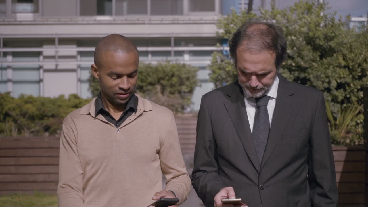 Focused men talking and walking with smartphones in city