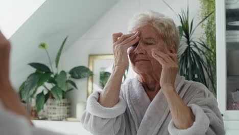 senior woman struggling with headache in bathroom in the morning