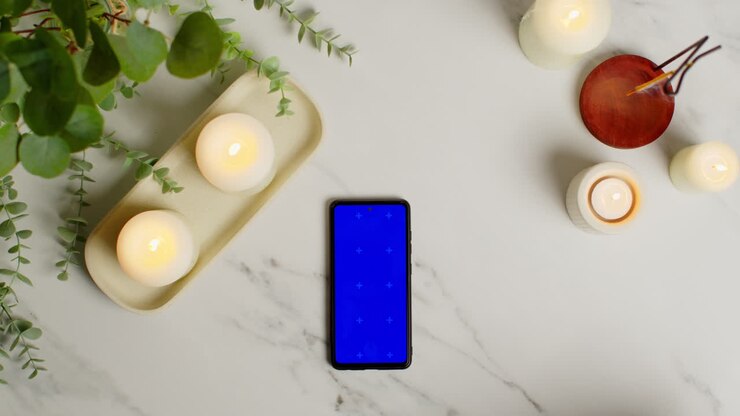 Overhead View Looking Down On Still Life Of Blue Screen Mobile Phone Lit Candles And Incense Stick With Green Plant And Towels As Part Of Spa Day Decor 2