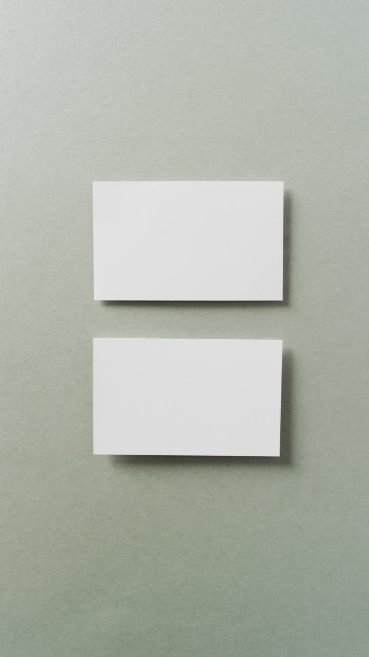 Vertical video of two white business cards arranged on grey background, copy space, slow motion