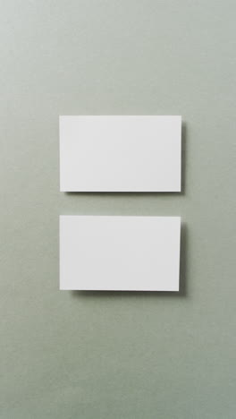 vertical video of two white business cards arranged on grey background, copy space, slow motion