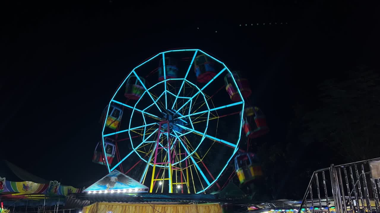 Colorful Ferris wheel glowing with neon lights spins at night in a festive carnival scene, perfect for travel, lifestyle, and event-related projects