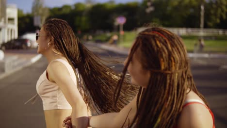 two happy women with dreads walking on the empty road and talking in summer. two hipster girls laughing and dancing during a