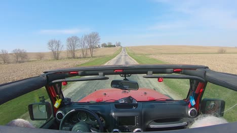 POV-while-a-white-haired-couple-are-driving-on-a-country-road-with-roof-off-of-their-vehicle