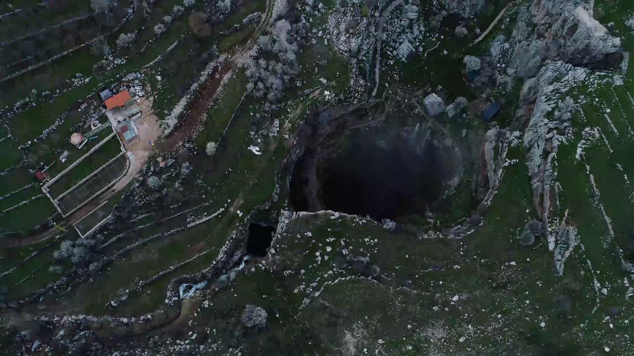 Aerial circle pan and pull back drone shot above dark rocky hole in landscape, Tannourine, Lebanon