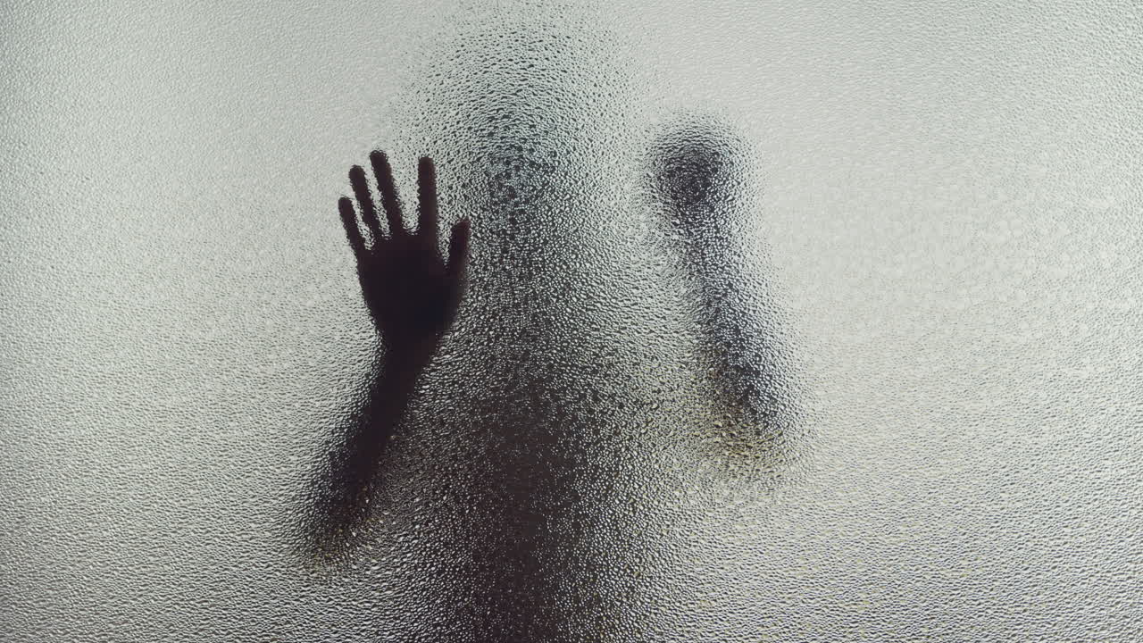 A female silhouette behind the frosted window slowly touches the glass