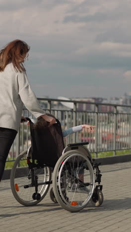 woman controls wheelchair with little girl spinning around. cheerful mother and daughter with disability enjoy walk in city on sunny spring day