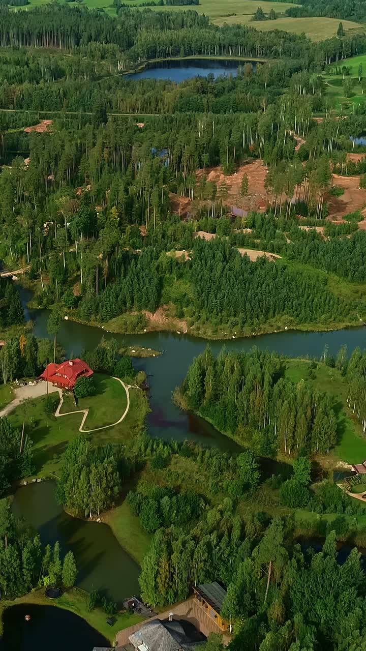 High aerial drone footage reveals the beautiful eco-village of Amatciems in Latvia, where modern houses are integrated into a stunning landscape of dense forests and pristine lakes