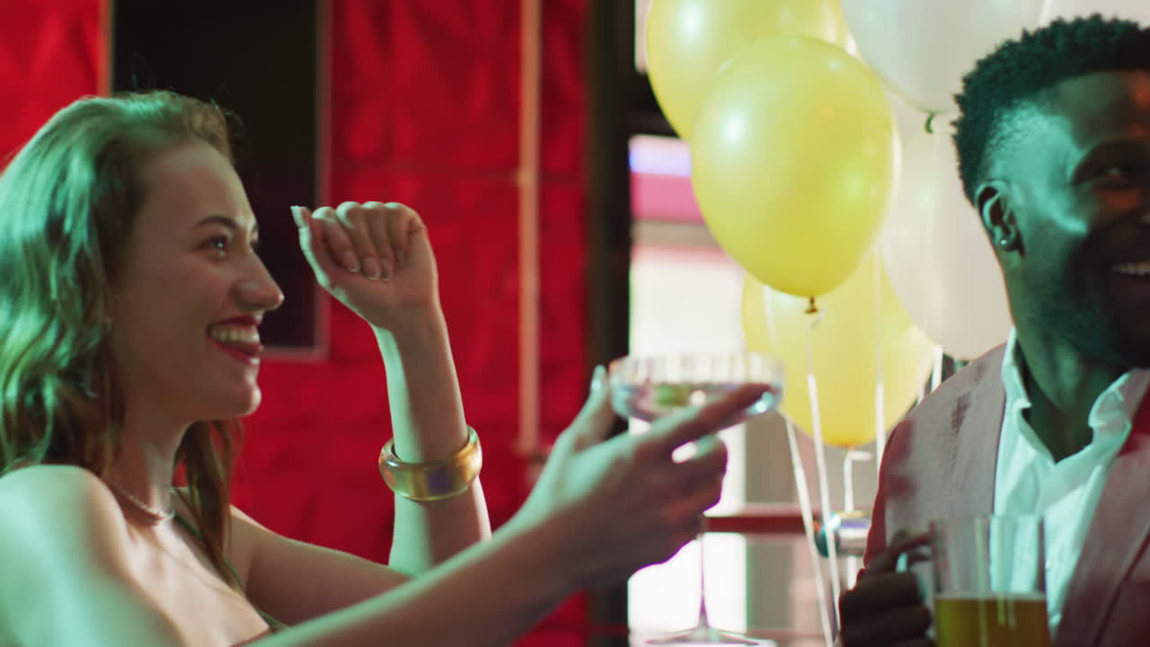 Video of diverse group of happy friends laughing, drinking and making a toast at a nightclub bar