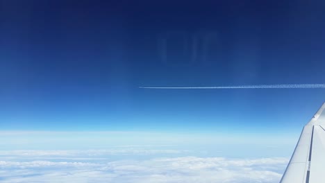 airplane flying above clouds with trail from the window with wing and horizont