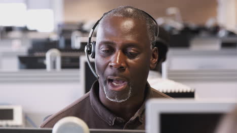 Mature-Businessman-Wearing-Telephone-Headset-Talking-To-Caller-In-Customer-Services-Department