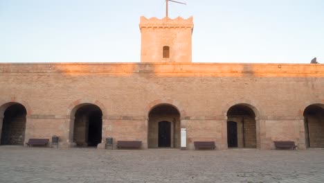 Leerer-Innenhof-Aus-Stein-Der-Burgmauer-Von-Montjuic-In-Barcelona,-Spanien-Bei-Sonnenuntergang-Mit-Klarem-Blauen-Himmel