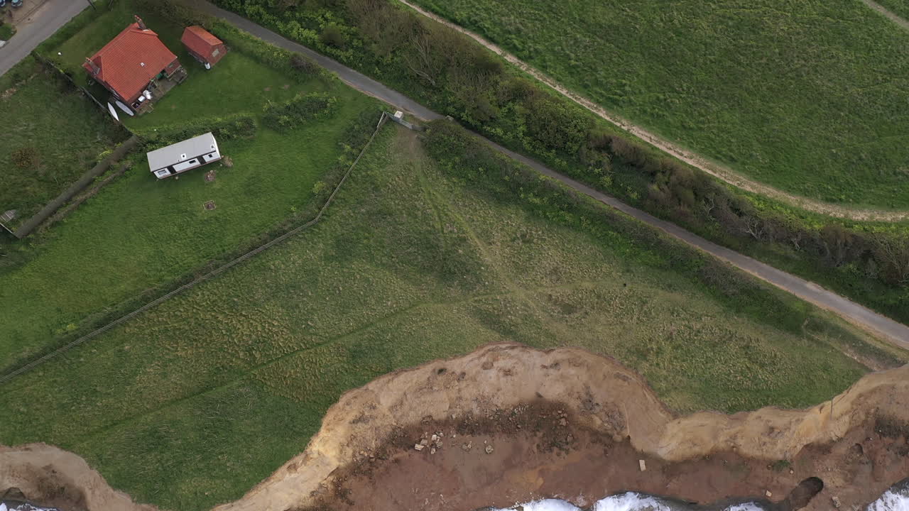 una toma aérea de un dron que comienza a mirar hacia abajo a la marea alta que golpea las defensas marinas y se desplaza hasta el pueblo de happisburgh, norfolk