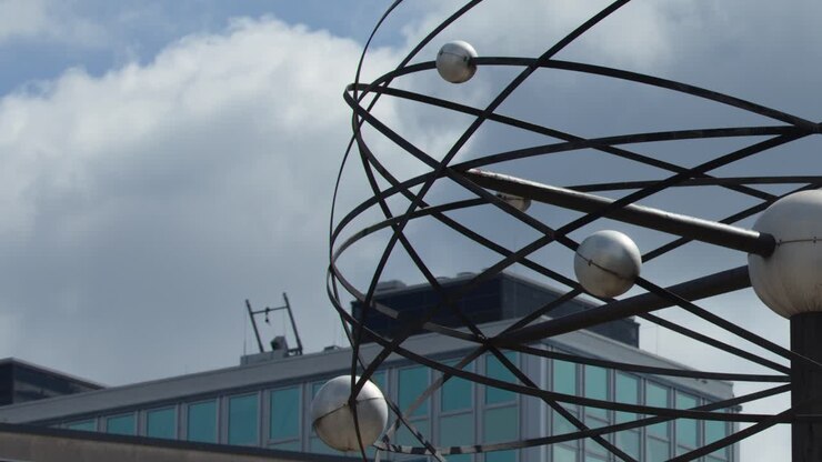 Scultura di una sfera metallica che ruota all'aperto, luce diurna nuvolosa, architettura urbana, primo piano, ripresa stabile