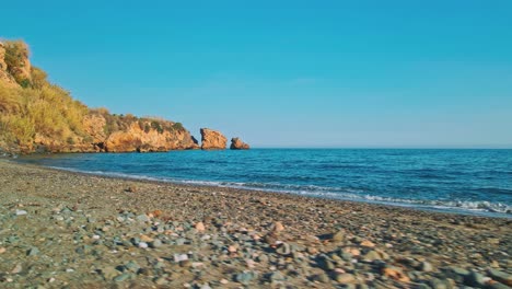 Empty-rocky-beach-with-drone-moving-into-the-sea