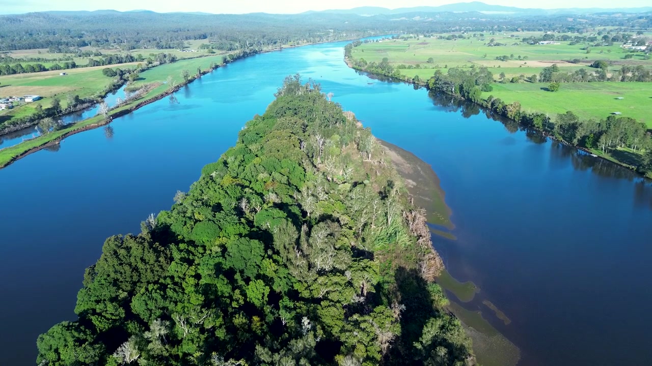 Paisagem aérea de drone da Reserva Natural da Ilha Coocumbac, coberta por dossel de floresta, ao longo do Rio Manning, com a paisagem rural de Taree na Costa Centro-Norte da Austrália, turismo.