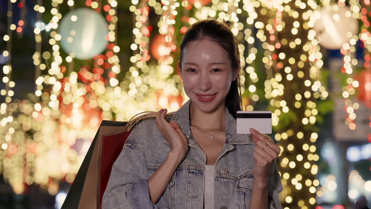 Woman holding shopping bags and a credit card in front of city lights