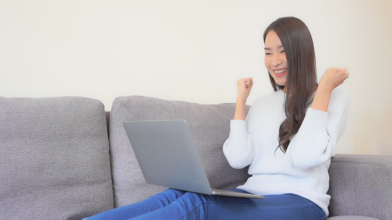 joven mujer asiática escribiendo en la computadora portátil, celebrando el éxito con el gesto de la mano sí