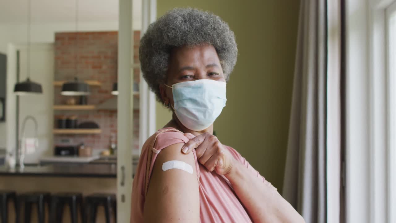 Felice donna anziana afroamericana con mascherina che mostra un cerotto sul braccio dopo la vaccinazione anti-Covid.