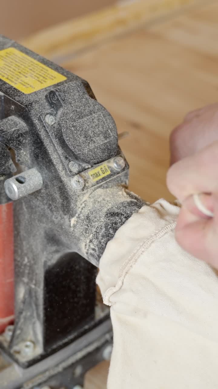 Person attaching dust collection bag to sanding machine during floor restoration, vertical