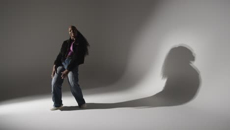 Full-Length-Studio-Portrait-Shot-Of-Young-Woman-Dancing-Casting-Shadow-With-Low-Key-Lighting-Against-Grey-Background