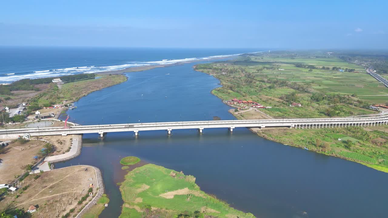 Aerial view of a white bridge crosses the river estuary to the wavy beach. Kretek II bridge and Depok Beach, Yogyakarta, Indonesia. 4K drone shot