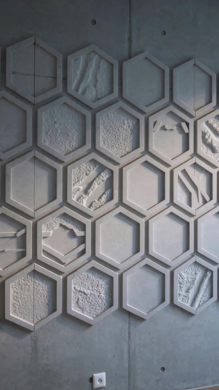 Video vertical: Cámara paneando desde la izquierda revelando paneles hexagonales texturizados en una galería, mostrando una toma de corriente