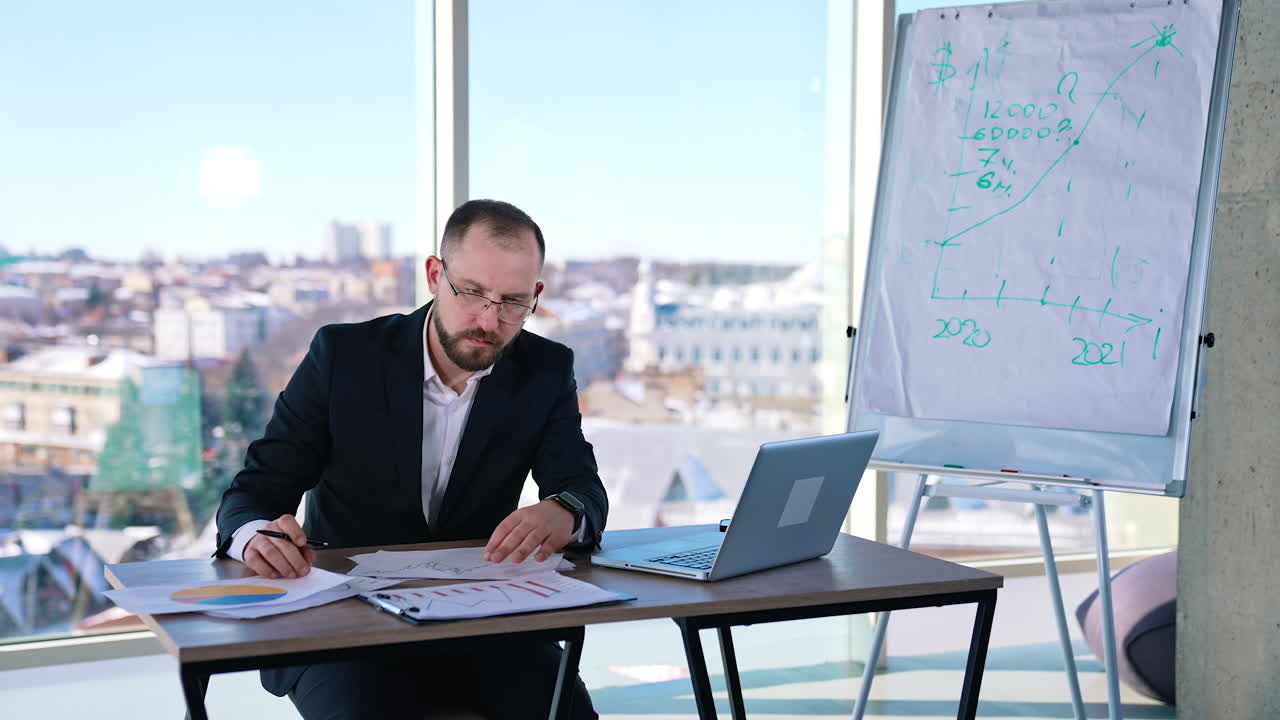 Serious businessman working indoors. Portrait of middle-aged man entrepreneur in glasses sitting at table and looking in papers in office room.