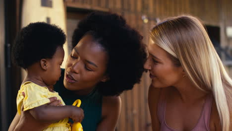 same sex family with two mums playing with young daughter and her toys outdoors at home