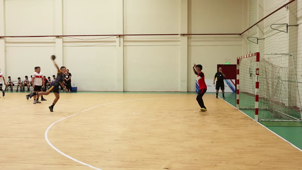 Editorial footage of a young handball player taking and scoring a penalty shot in an official match. The referee validates the goal immediately after the successful shot