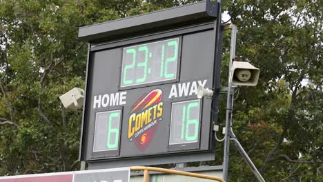Outdoor digital scoreboard displays rugby match time, team names, and scores in natural daylight