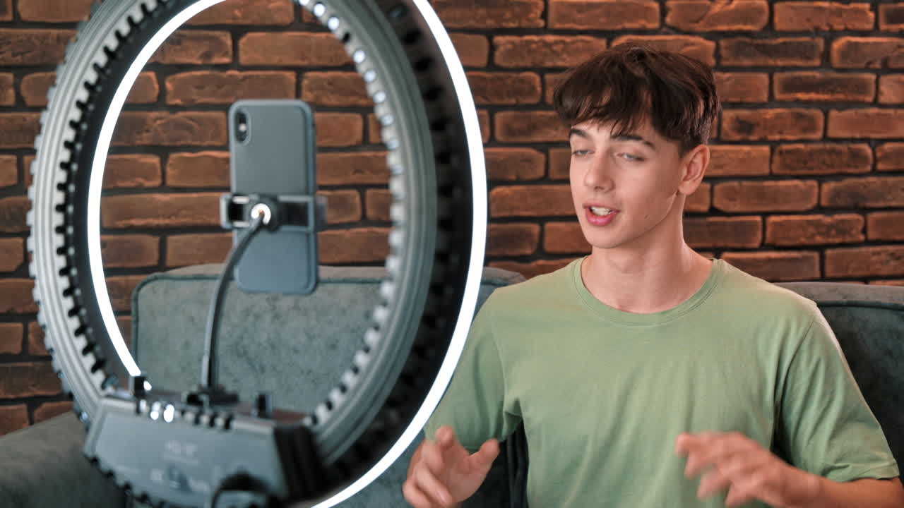 A young smiling man blogger influencer talking and shooting himself on smartphone on a tripod with ring light in a studio