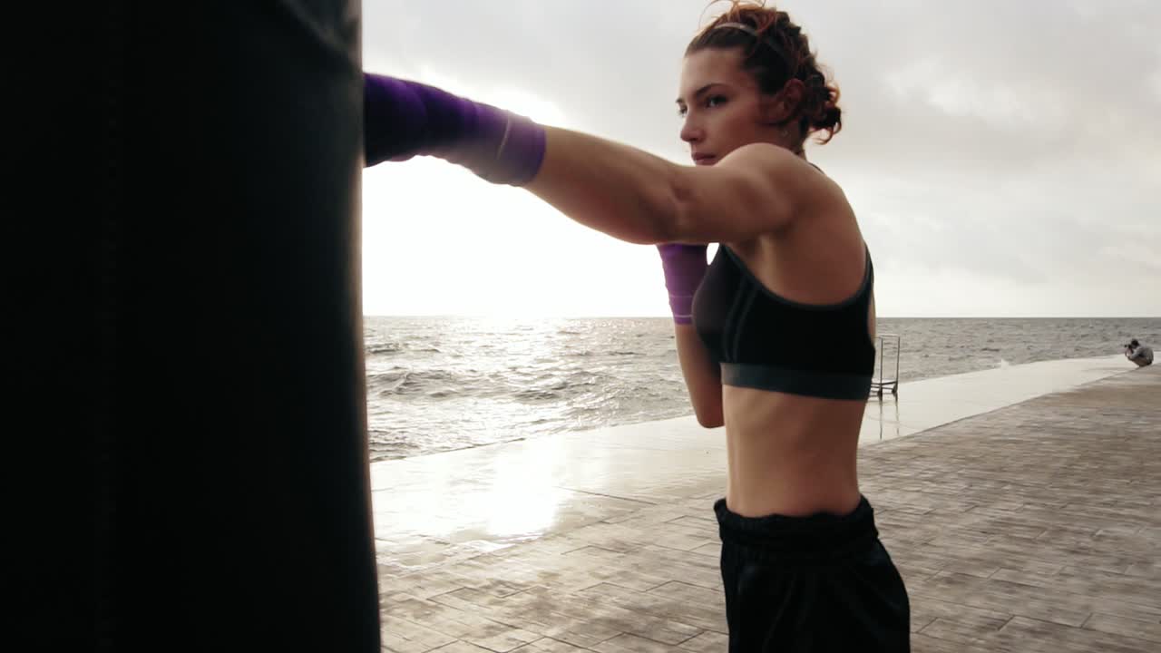 vista de cerca de una mujer joven entrenando con la bolsa de boxeo contra el hijo. sus manos están envueltas en cintas de boxeo púrpura