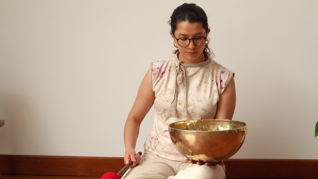 Female figure kneeling while striking a large Tibetan bowl with a padded mallet