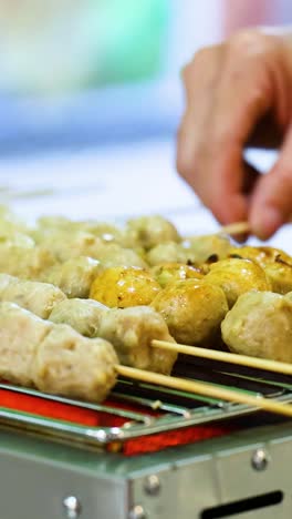 manos asando albóndigas asadas en un puesto de mercado