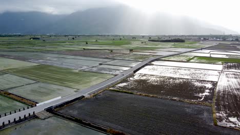 La-Luz-Del-Sol-Brilla-Sobre-Los-Arrozales-Húmedos-Con-Montañas-Al-Fondo,-Un-Tranquilo-Paisaje-Rural.