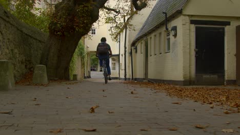 Rising-Shot-of-Cyclist-Riding-Through-Scenic-Alleyway-In-Oxford