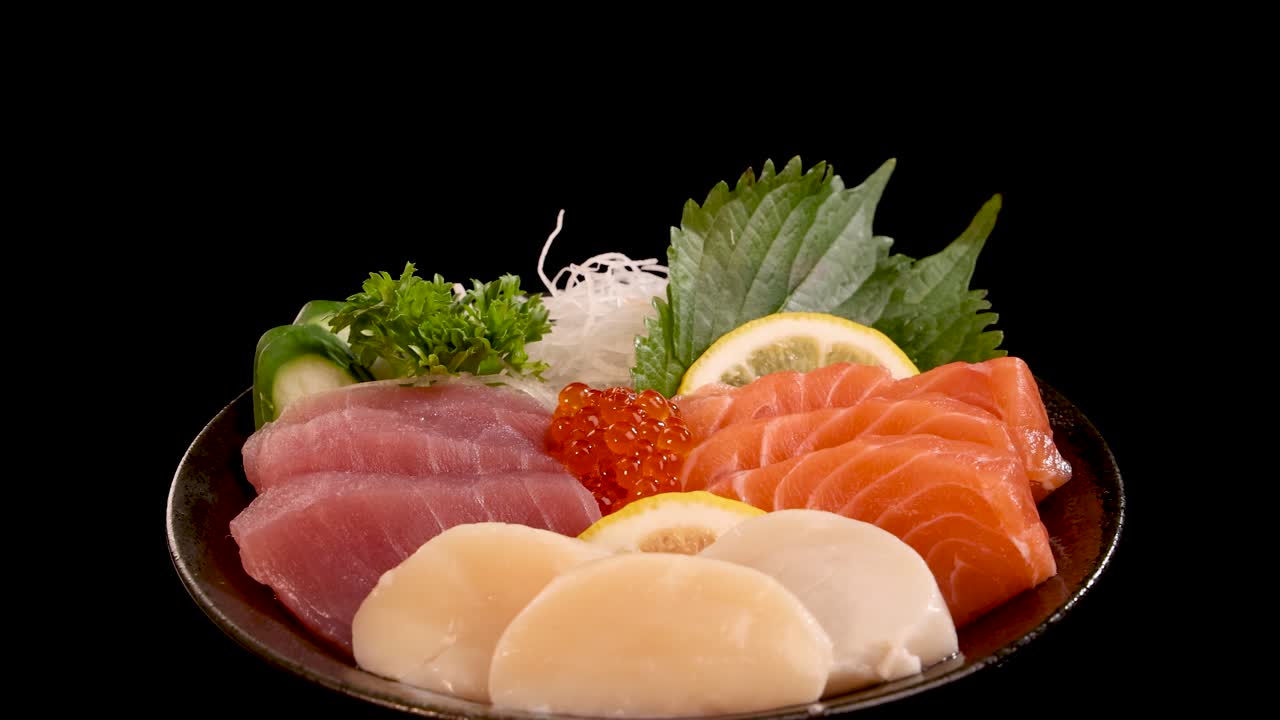 Assorted sashimi and sushi, including salmon, tuna, scallop, and salmon roe, presented on a plate with garnishes, smoothly rotating under studio lighting