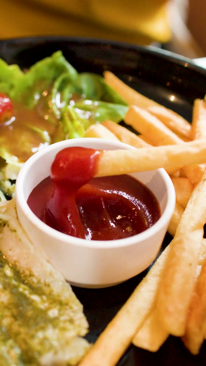 Primo piano di una mano che intinge una patatina fritta croccante in una ciotola di ketchup.