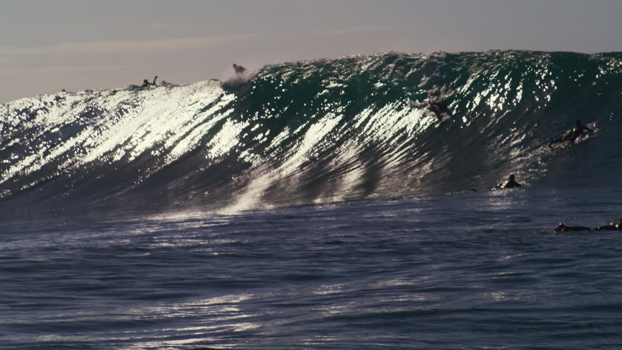 los surfistas apenas logran superar la cresta de la ola mientras el agua choca en una brillante exhibición de fuerza.