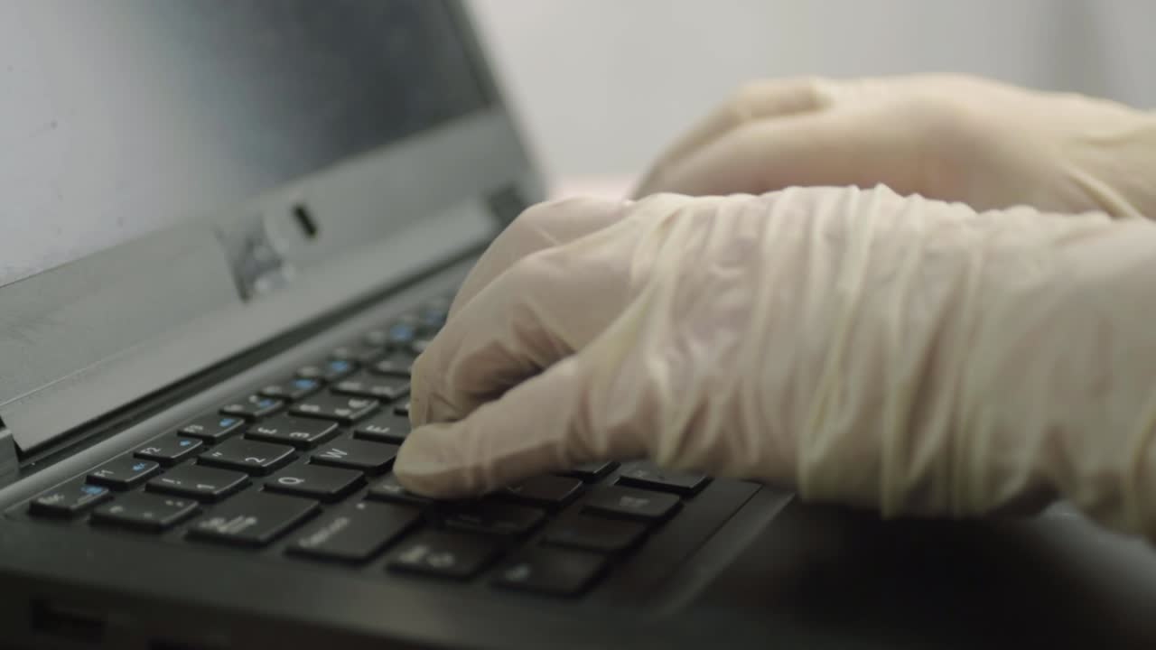 mano con guantes higiénicos escribiendo en el teclado de una computadora portátil plano medio
