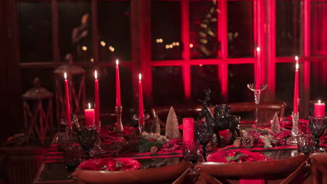 celebratory table laid for christmas dinner celebrations. lots of candles, fir-tree branches and cones, beads and beautiful crockery. blurred backdrop.