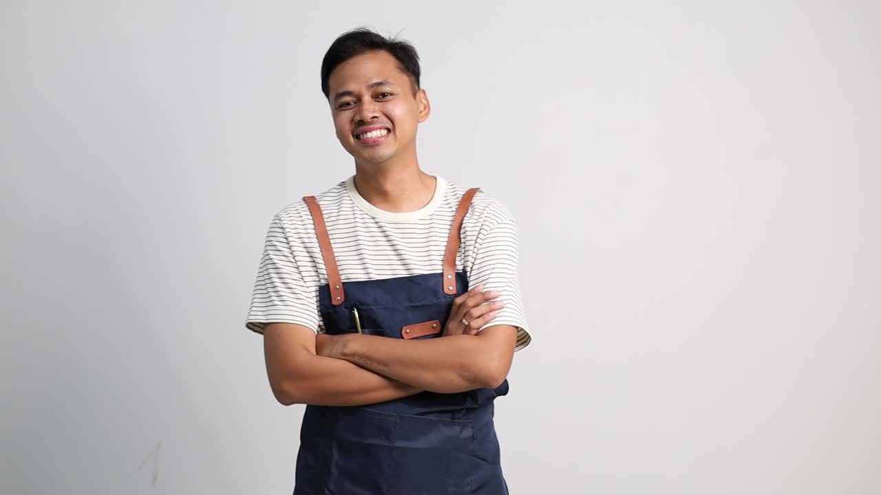 Seorang pria muda tampan dan percaya diri mengenakan celemek dengan tangan dilipat