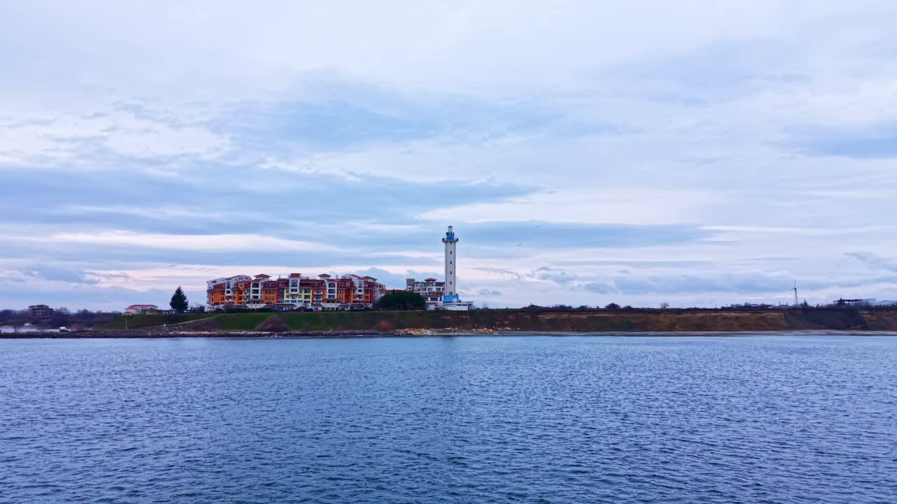 Vista di una zona costiera con edifici e un faro vicino alla riva durante una giornata nuvolosa
